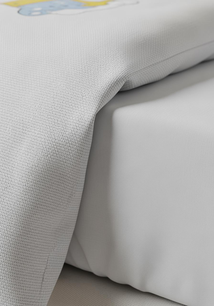 Vue macro des textures d'une parure de lit pour enfant, montrant le tissu d'une couette et d'un drap-housse.
