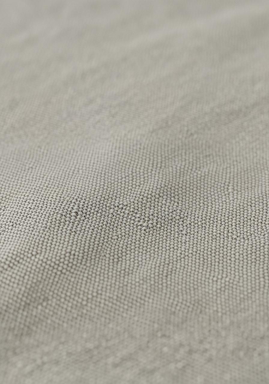 Vue macro d'un tissu en lin lavé, montrant la trame aérée des fibres qui suggère sa respirabilité.