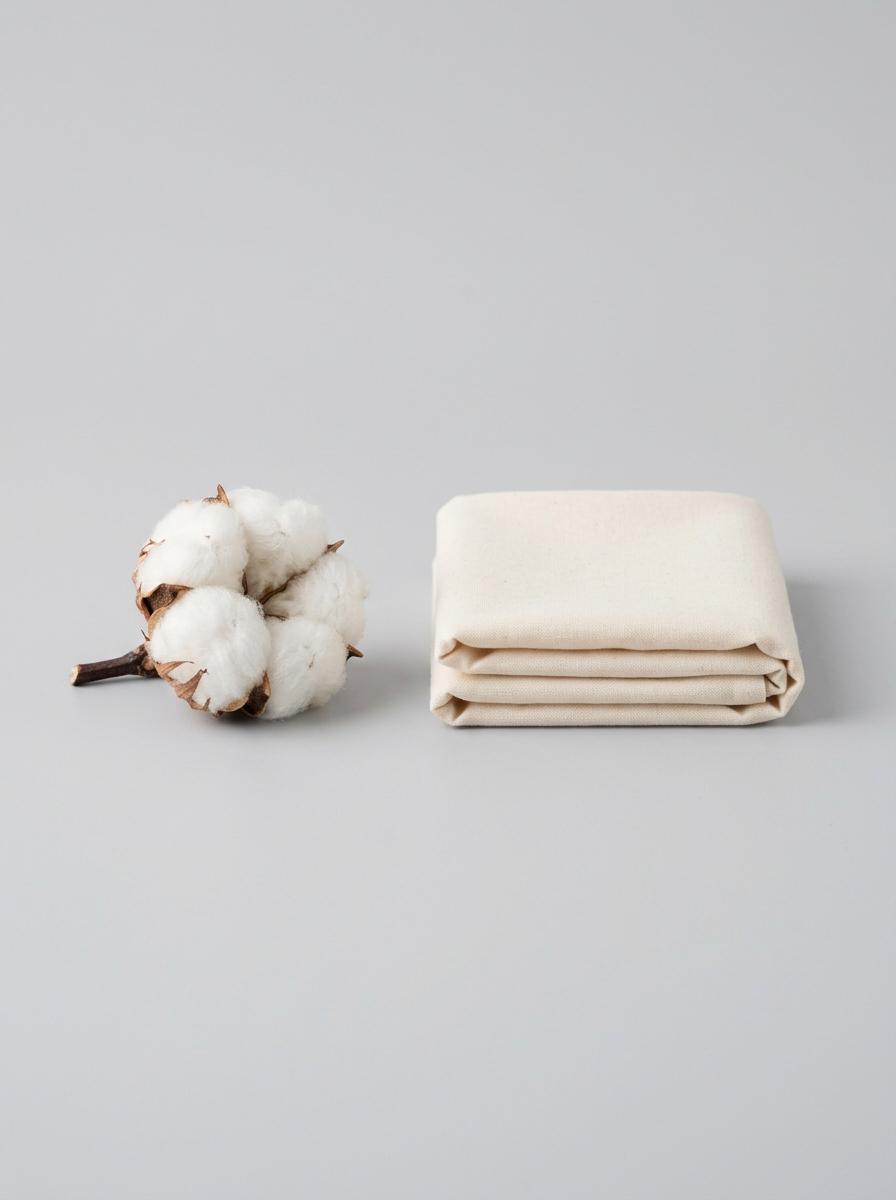 Une bourre de coton brut placée à côté d'une pile de tissu de coton plié, illustrant la transformation de la fibre en textile.