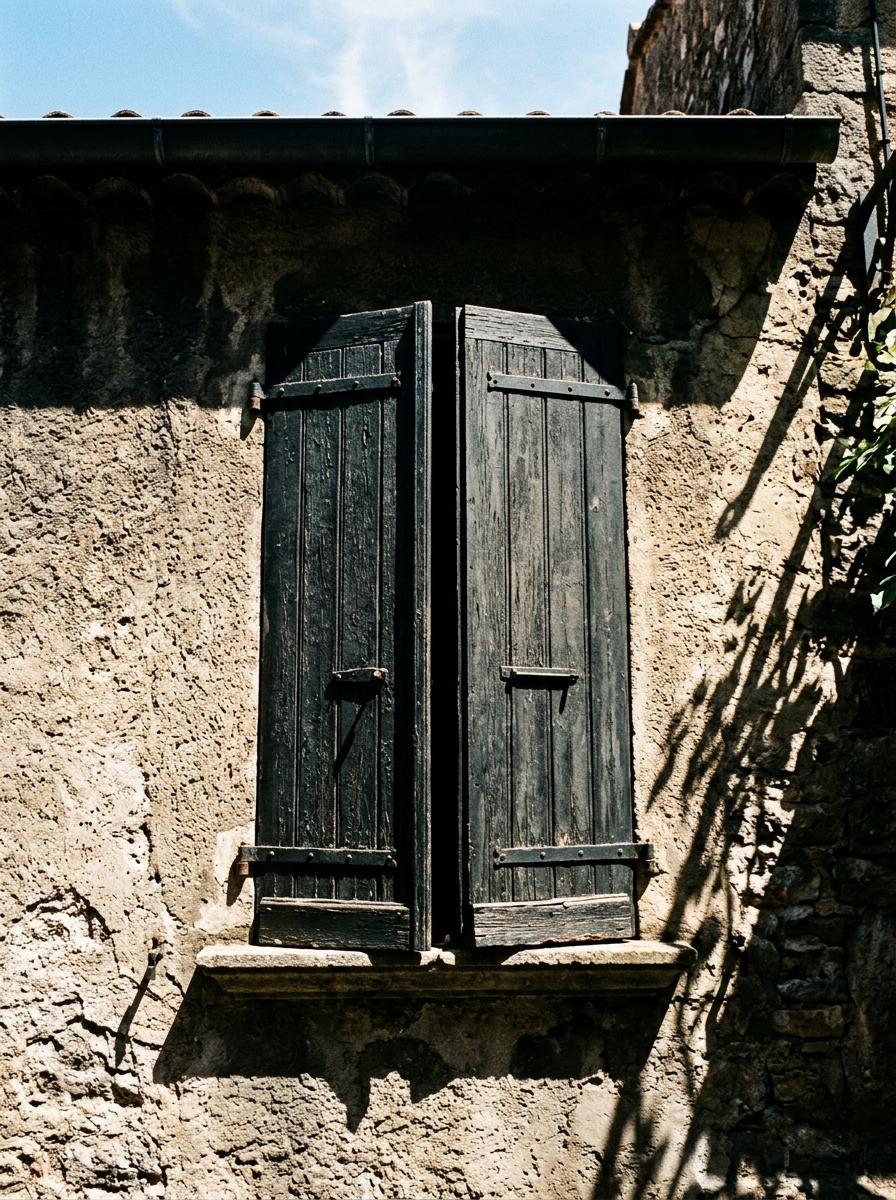 Des volets en bois sur une façade ensoleillée, presque fermés pour bloquer la chaleur et créer une forteresse contre la canicule.