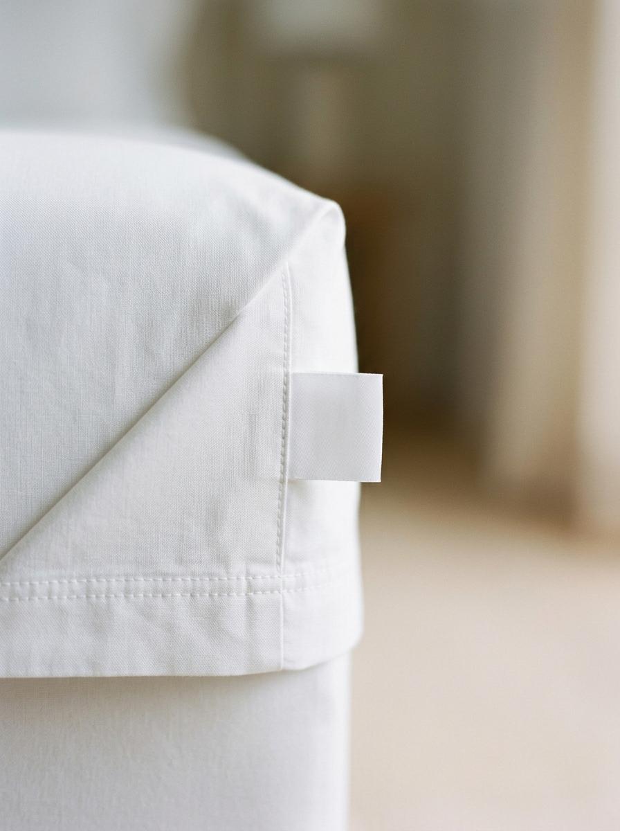 Gros plan sur le coin d'un drap blanc de haute qualité, montrant une couture parfaite et un tissu pur, symbolisant la certification et la sécurité.