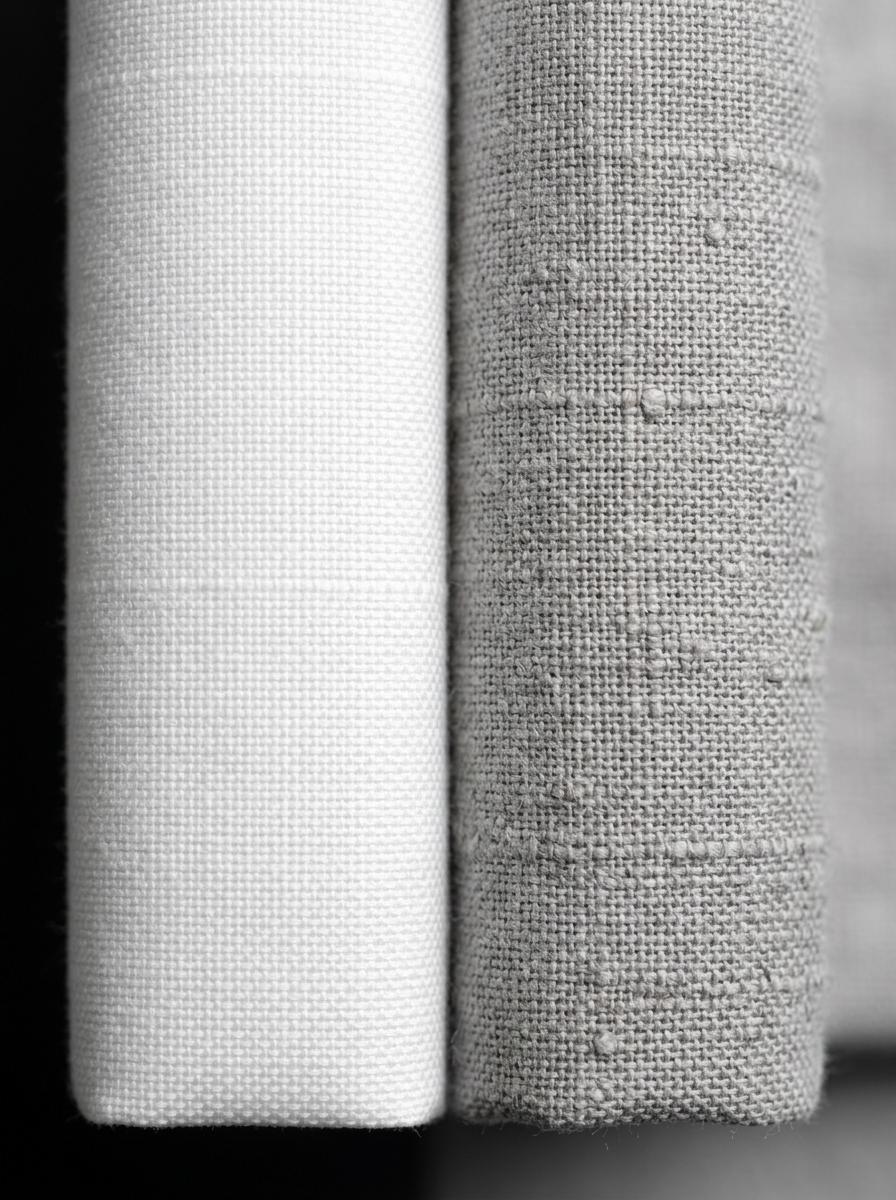 Vue macro comparant la texture d'un tissage de percale de coton blanc et mat à celle d'un lin lavé gris et texturé.
