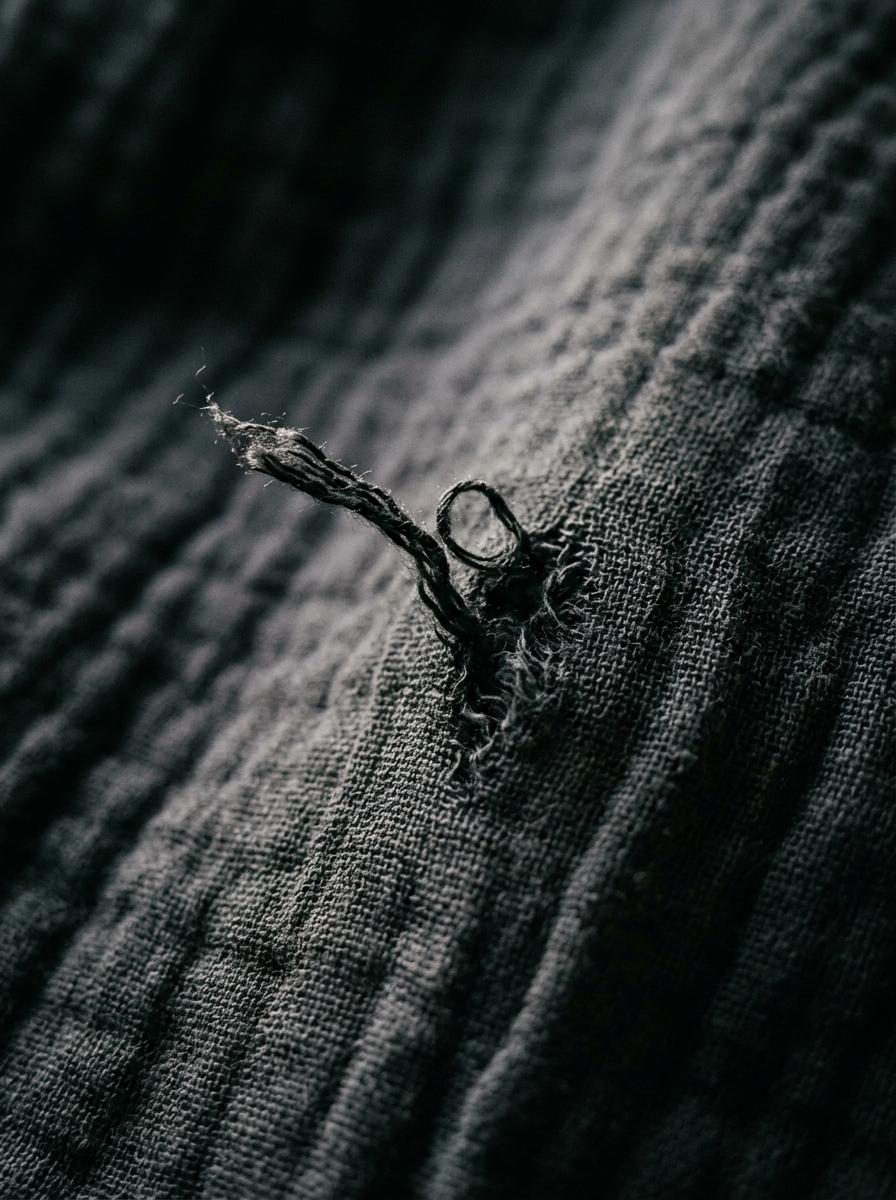 Gros plan sur un accroc, un fil tiré, sur un tissu en gaze de coton de couleur sombre pour illustrer un problème courant.