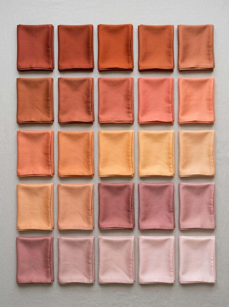 Vue de dessus d'une collection de taies d'oreiller en satin de coton, arrangées en un dégradé de couleurs allant de la terracotta au rose poudré.