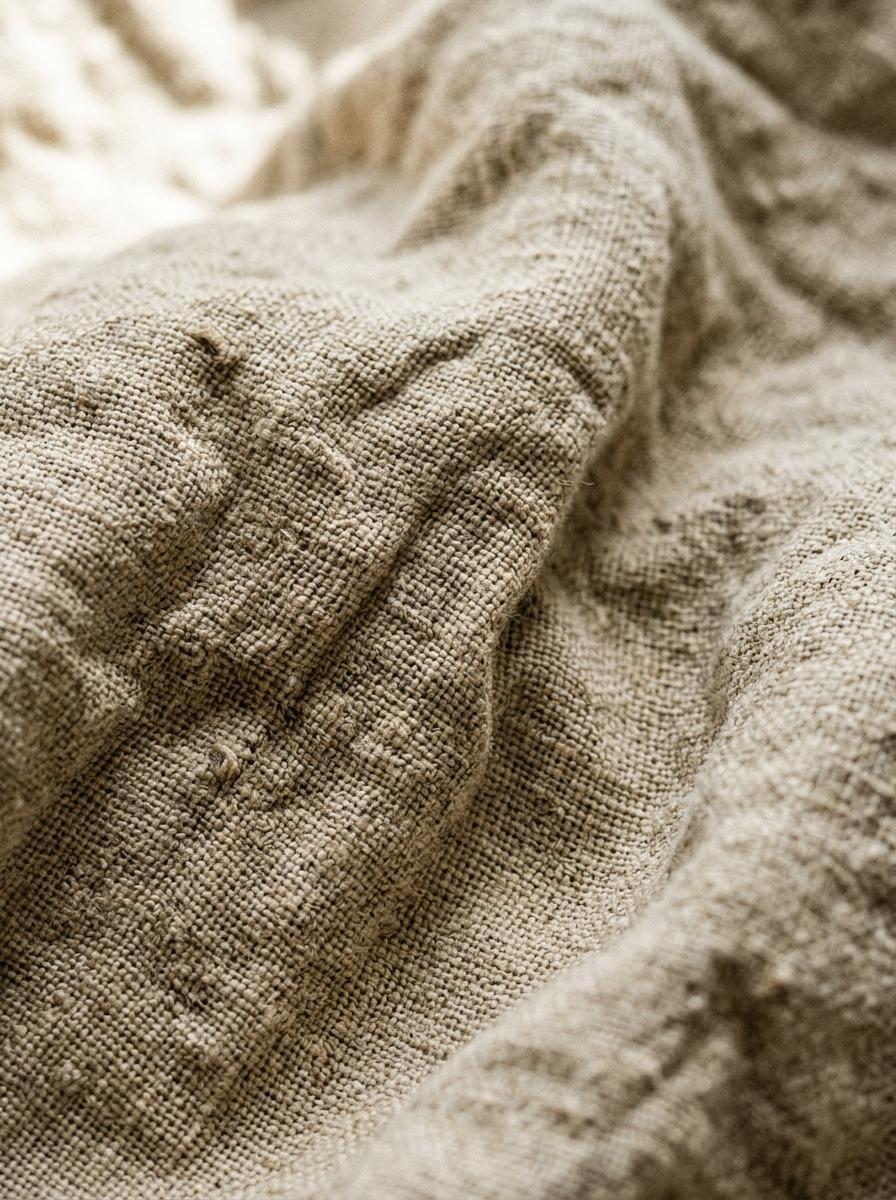 Une photo macro de la texture d'un tissu en lin lavé de couleur avoine, montrant le détail des fibres et des plis naturels.