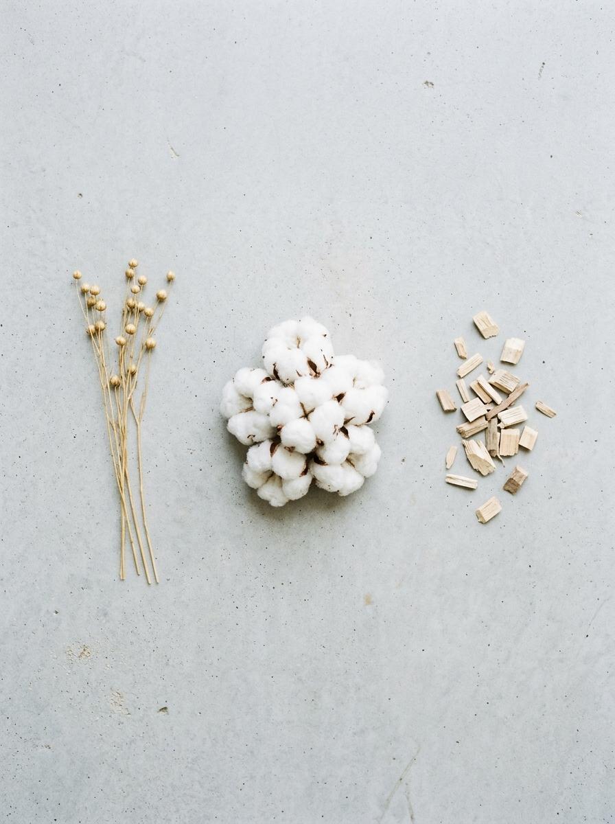 Vue de dessus des matières premières pour tissus apaisants : des bourres de coton bio, des tiges de lin et des copeaux d'eucalyptus.