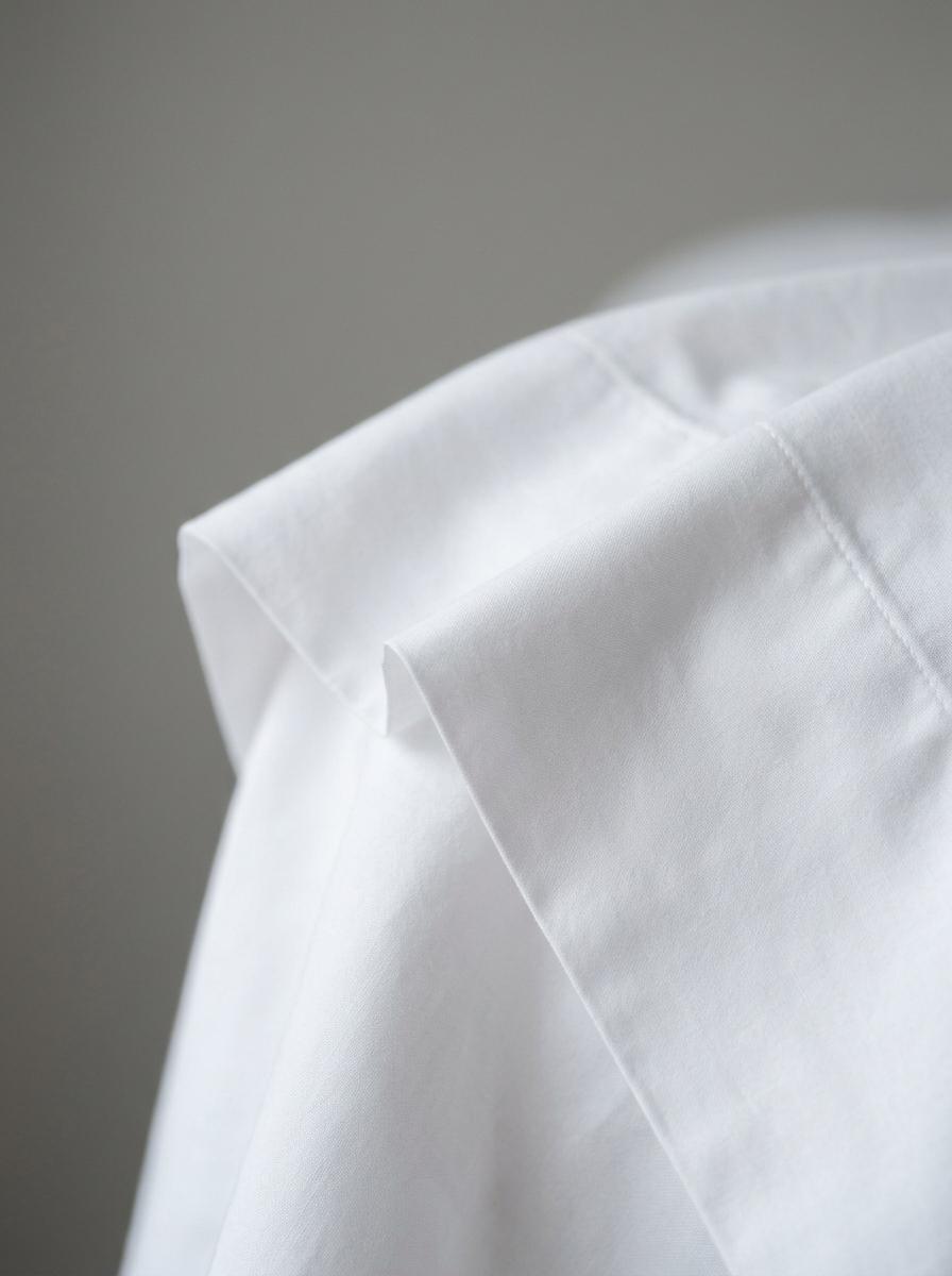 Gros plan sur un drap en percale de coton blanc, mettant en évidence sa texture nette et son aspect 'craquant' à travers des plis définis.