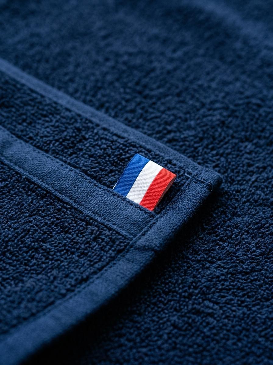 Gros plan sur le coin d'une serviette de qualité avec une petite languette ruban tricolore, symbolisant un label de garantie contrôlée comme 'Origine France Garantie'.