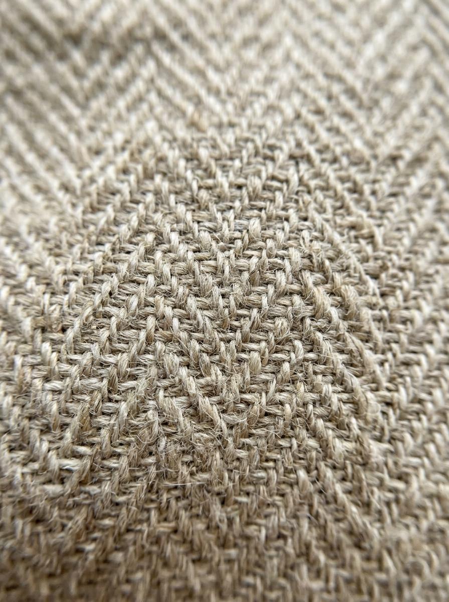 Macro photographie d'un tissage en chevron sur un tissu en lin épais, montrant la complexité et la qualité des fibres.
