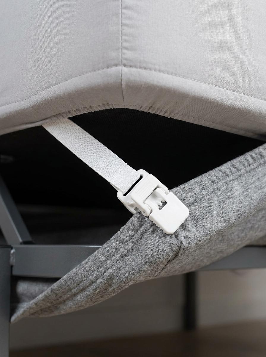 Gros plan sur un tendeur de drap avec une pince en plastique, solidement attaché au bord d'un drap-housse sous un matelas pour le maintenir en place.