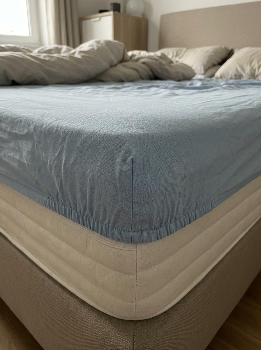 Le coin d'un drap-housse bleu clair qui est visiblement trop petit et étiré sur un matelas épais, sur le point de sauter.