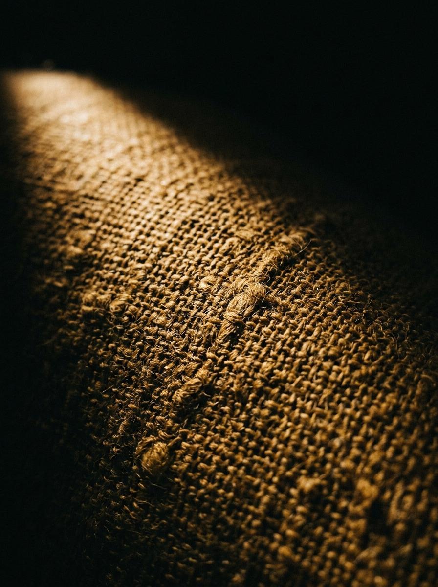Macro photographie de la texture d'un tissu en lin de couleur ocre, mettant en évidence le tissage et les fibres.