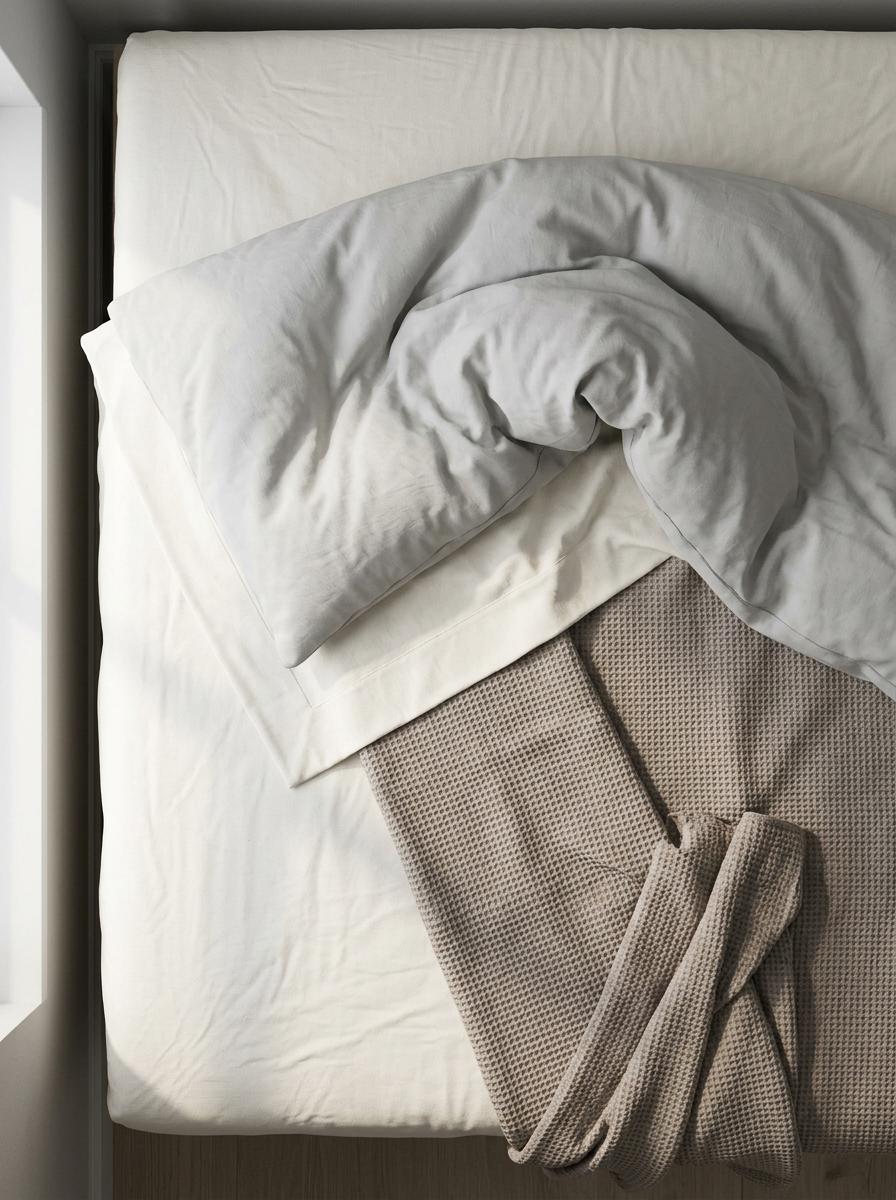 Vue du dessus des couches du lit : drap-housse, drap plat, couverture et couette partiellement rabattus.